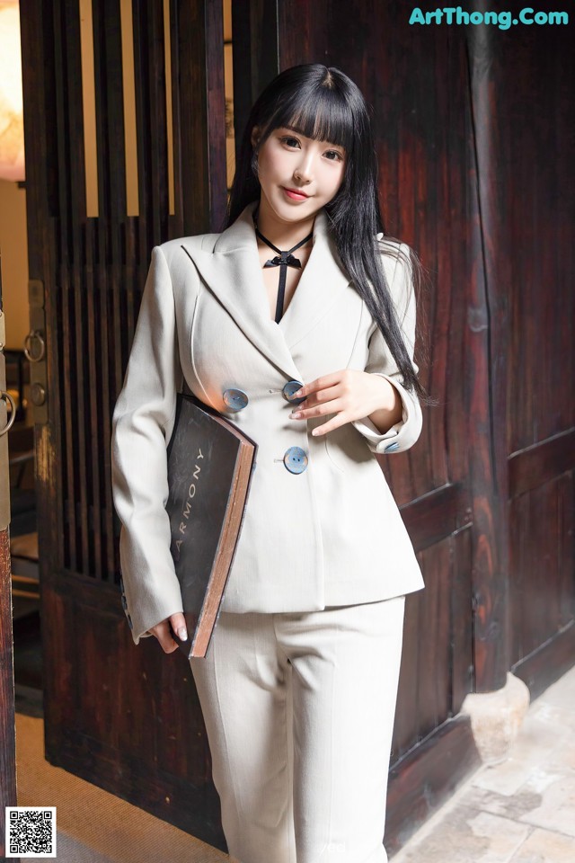 A woman in a beige suit holding a book.