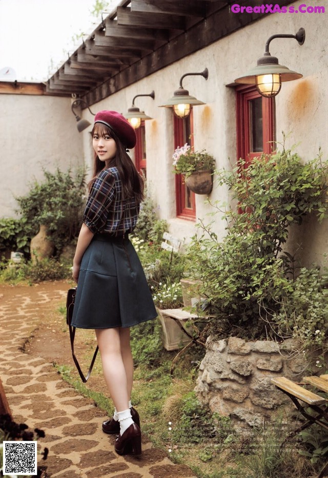 A woman in a plaid shirt and skirt standing in front of a building.