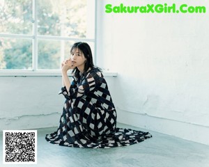 A woman in a black dress sitting on a window sill.