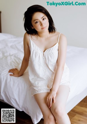 A woman in a black tank top and orange skirt leaning against a wall.