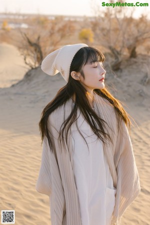 A woman in a white dress sitting on a sand dune.