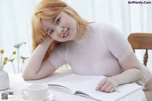 A woman in a white bodysuit sitting at a table.