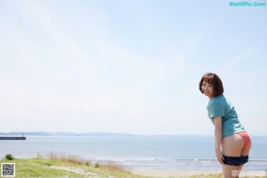 A woman in a pink bikini standing on a beach with her arms outstretched.