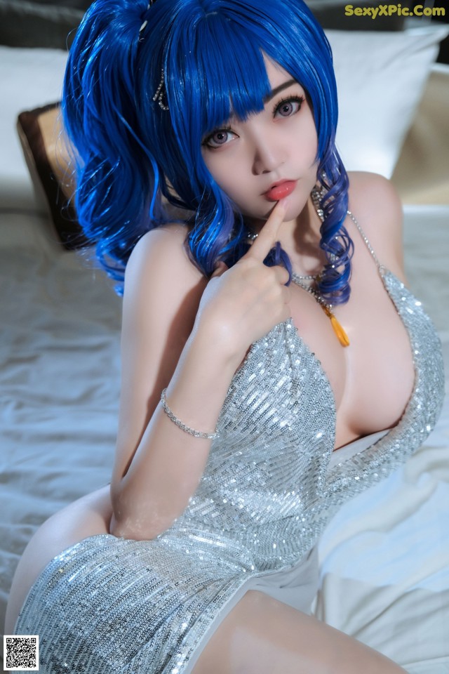 A woman with blue hair sitting on a bed.