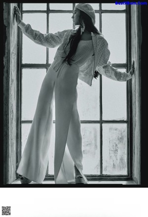 A woman sitting on a stool wearing white pants and a colorful top.