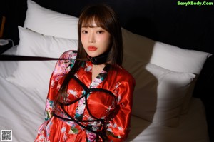 A woman in a red kimono sitting on a bed.