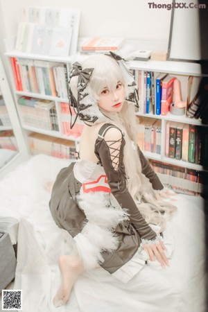 A woman in a maid outfit sitting on a bed.