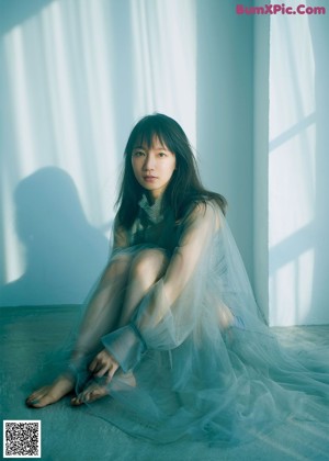 A woman sitting on a window sill wearing a blue sweater.