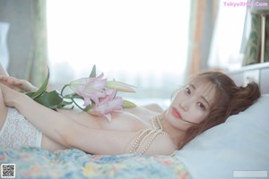 A woman sitting on top of a bed holding a flower.