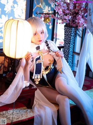A woman sitting on a bed next to a lamp.