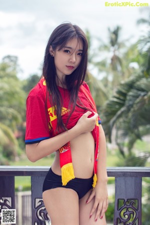 A woman in a red shirt and black panties posing for a picture.