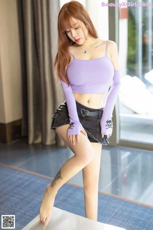 A woman in a purple top and black skirt posing for a picture.